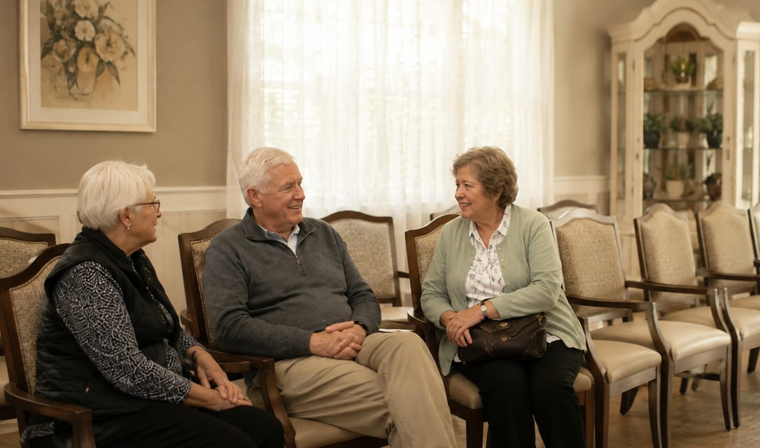 Three residents sitting together in the front sitting room at Sanford Place, turned toward each other mid-conversation.